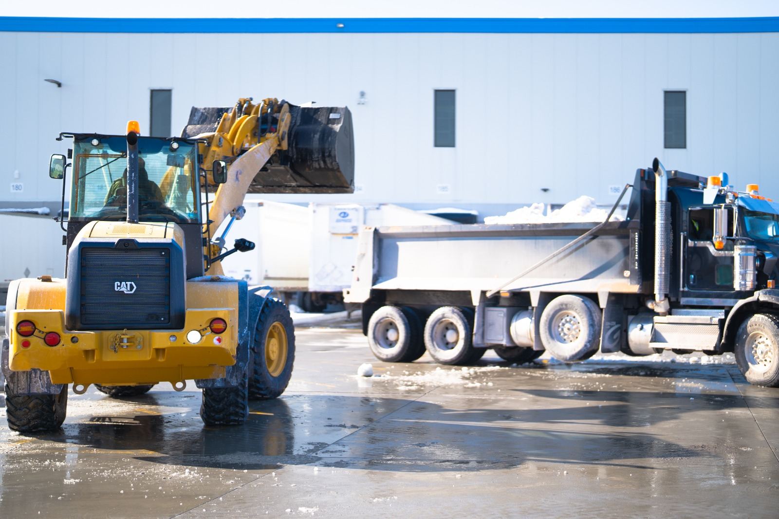 Spartan loader loading snow into a dump truck at a distribution facility
